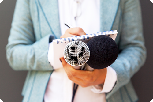 Foto einer Person mit zwei Mikrofonen und einem Notizblock in der Hand